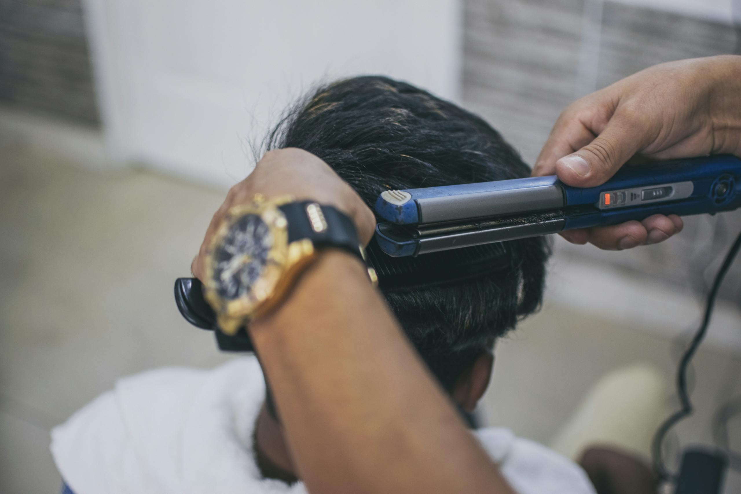 Close-up of a hairdresser styling a client's hair using a straightener in a barbershop.
