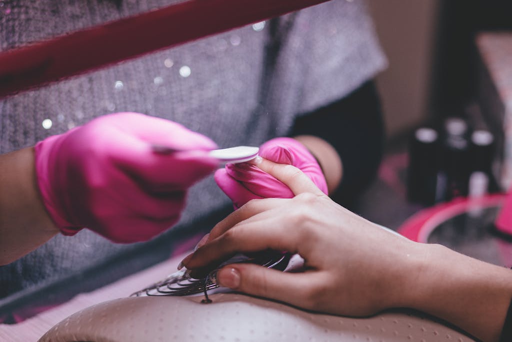 Close-up of a professional manicure session with pink gloves and a nail file in an indoor salon.